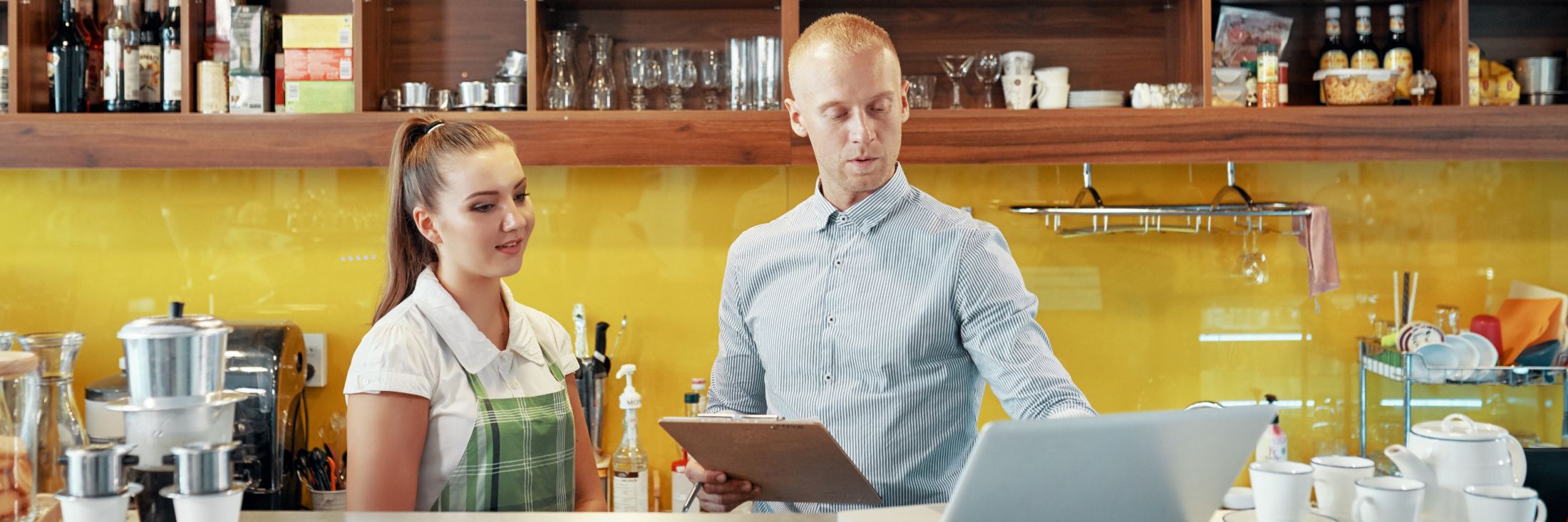 Two staff behind a cafe counter, one working at a laptop